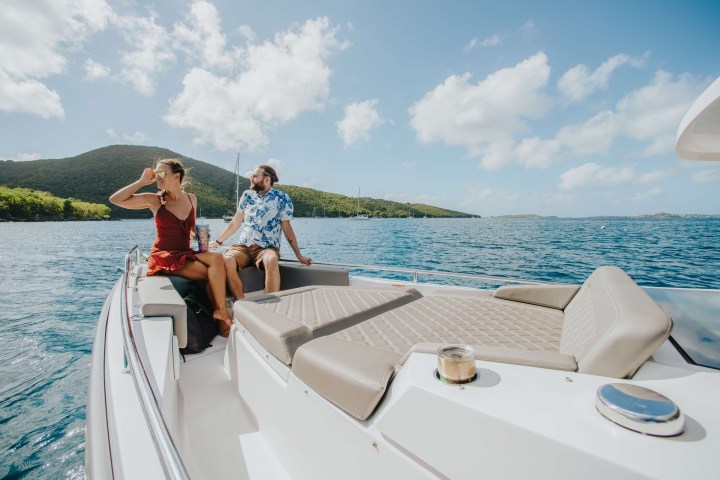 Couple relaxing on a boat with scenic ocean and hills in the background.