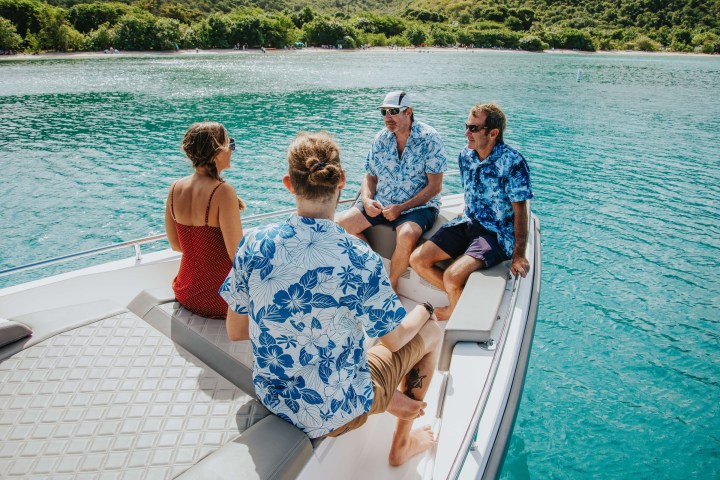 Four people on a boat in blue water, three wearing floral shirts.