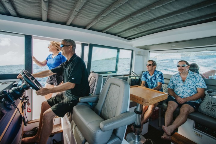 Four people in a boat cabin sailing, with ocean visible through windows.